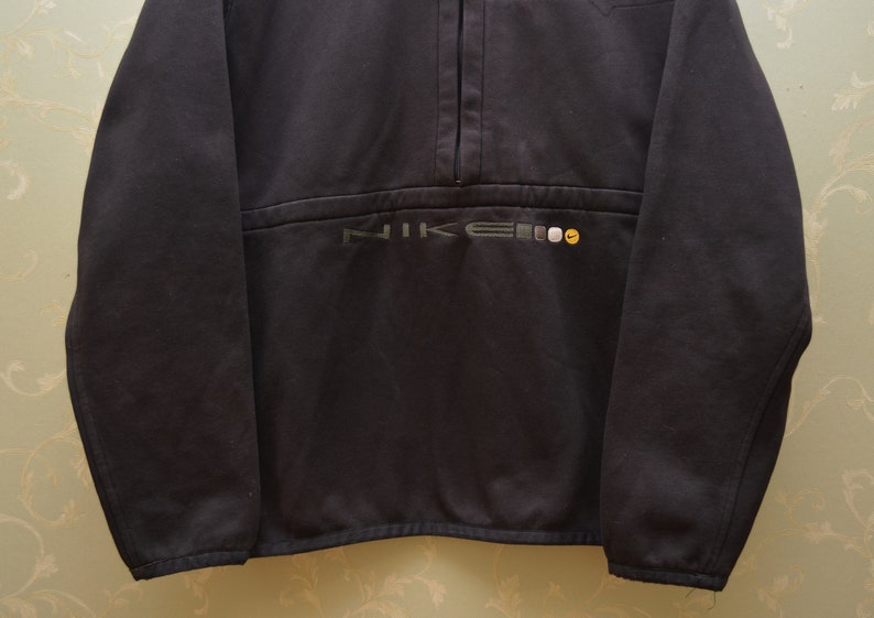 May include: A black Nike fleece pullover with a half-zip closure and the word "NIKE" embroidered in grey and yellow on the front.