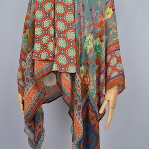 May include: A vibrant, patterned shawl with floral and geometric motifs. The shawl displays orange, teal, and green tones. The fabric seems lightweight and flowing, ideal for layering. The shawl is displayed on a mannequin.