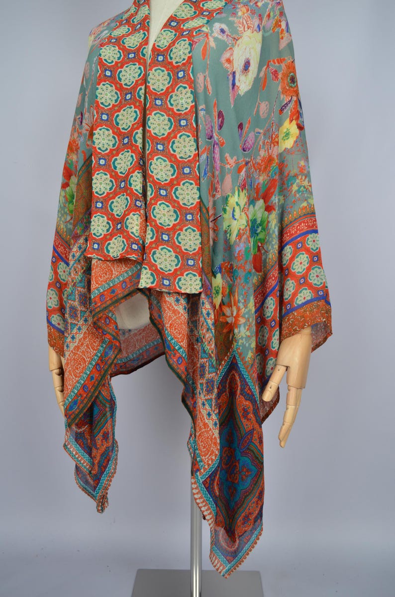 May include: A vibrant, patterned shawl with floral and geometric motifs. The shawl displays orange, teal, and green tones. The fabric seems lightweight and flowing, ideal for layering. The shawl is displayed on a mannequin.
