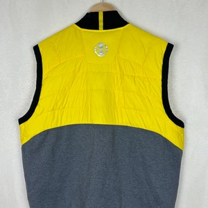 Puede incluir: Un chaleco sin mangas amarillo y gris con una cremallera negra y un cuello negro. El chaleco tiene un logotipo en la espalda que dice "Team".