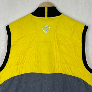 Puede incluir: Chaleco sin mangas amarillo y gris con cremallera negra y cuello negro. El chaleco tiene un logotipo en la espalda que dice "Polo Ralph Lauren".