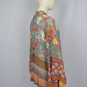 May include: A floral print kimono-style top in shades of teal, orange, and yellow. The lightweight fabric features a vibrant pattern of flowers and leaves. The kimono has wide sleeves and a flowing silhouette, perfect for layering.