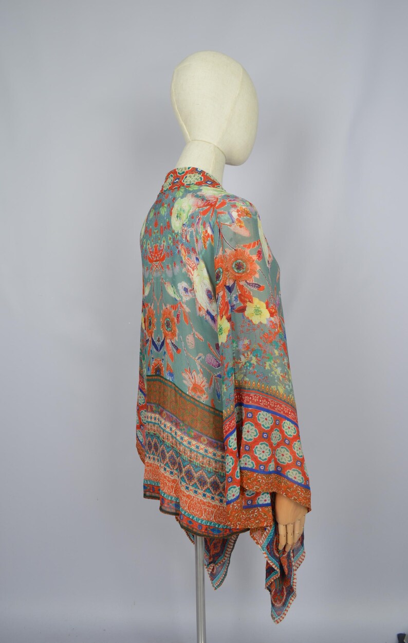 May include: A floral print kimono-style top in shades of teal, orange, and yellow. The lightweight fabric features a vibrant pattern of flowers and leaves. The kimono has wide sleeves and a flowing silhouette, perfect for layering.