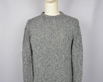 May include: A gray knitted sweater with a crew neck and long sleeves. The sweater is made of a soft, textured yarn.