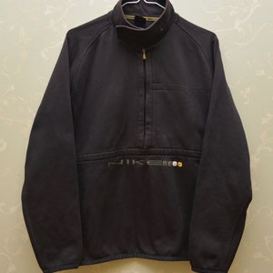 May include: A black Nike fleece jacket with a half-zip closure and a small pocket on the left chest. The Nike logo is embroidered in gray and yellow on the bottom front of the jacket.