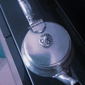 May include: A silver teapot with a decorative floral design on the lid. The teapot has a spout and a handle. The teapot is engraved with the text "Made in England".