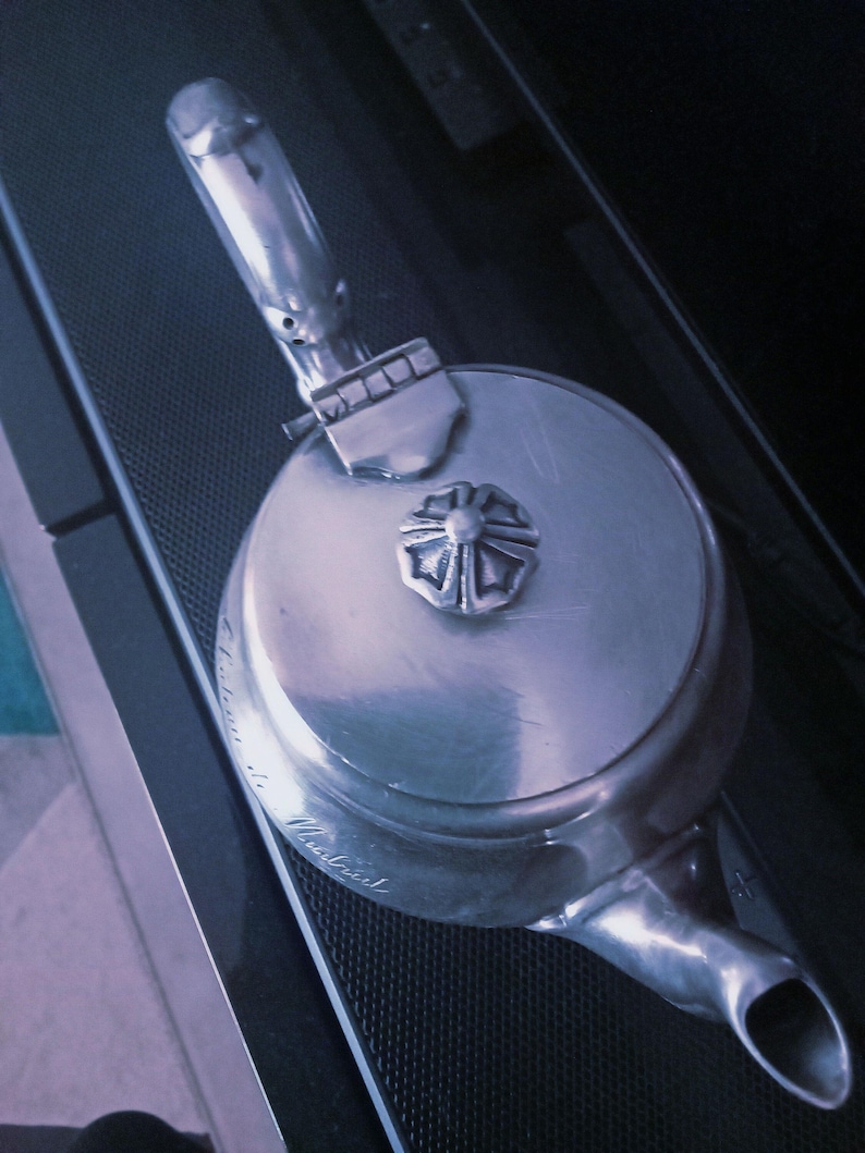 May include: A silver teapot with a decorative floral design on the lid. The teapot has a spout and a handle. The teapot is engraved with the text "Made in England".
