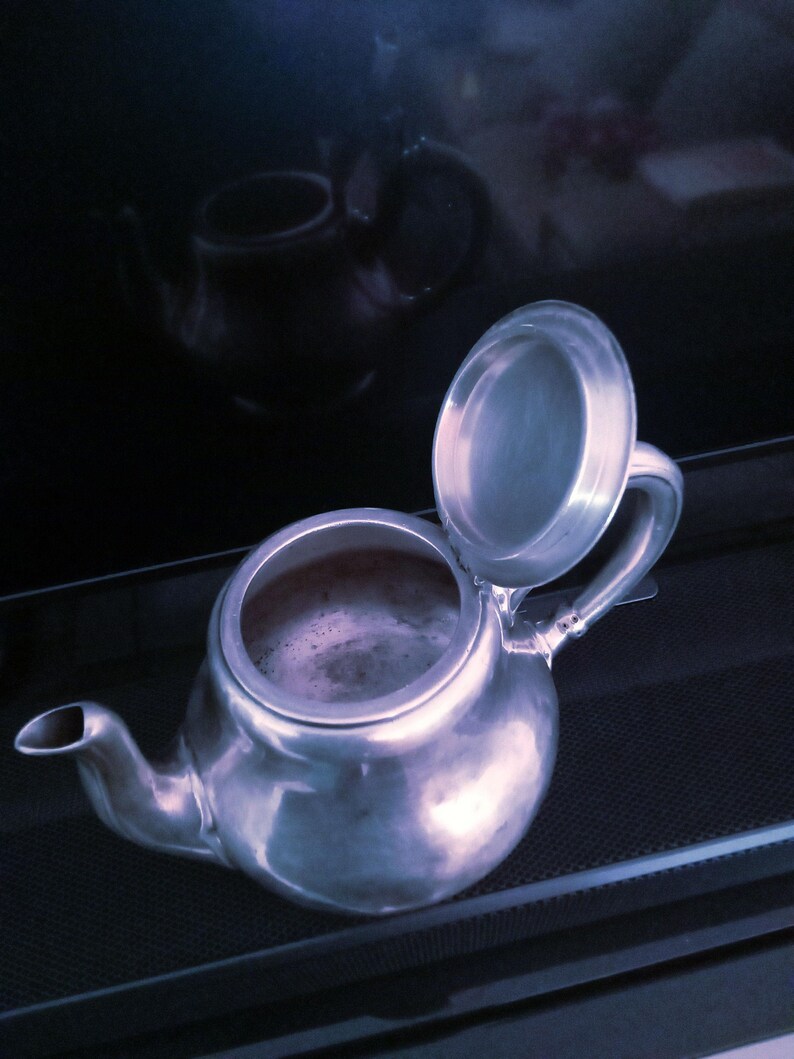 May include: A silver teapot with a lid that is open. The teapot is sitting on a black surface.