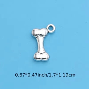 Könnte beinhalten: Silberfarbener Hundeknochen-Anhänger aus Metall mit einem Ring oben. Der Anhänger ist 1,7 cm x 1,19 cm groß.