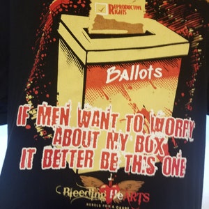 May include: Black t-shirt featuring a red and yellow graphic of a ballot box with the text "Reproductive Rights" and "Ballots". The text "If men want to worry about my box it better be this one" is printed below the graphic. The graphic is surrounded by red and yellow splatter paint. The text "Bleeding Hearts Rebels for a Cause" is printed below the graphic.