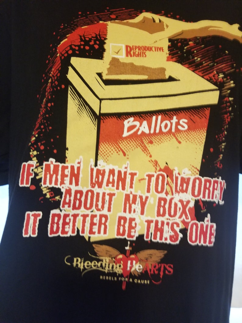 May include: Black t-shirt featuring a red and yellow graphic of a ballot box with the text "Reproductive Rights" and "Ballots". The text "If men want to worry about my box it better be this one" is printed below the graphic. The graphic is surrounded by red and yellow splatter paint. The text "Bleeding Hearts Rebels for a Cause" is printed below the graphic.