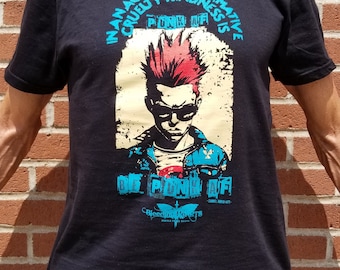 May include: Black t-shirt featuring a graphic of a punk rock character with red hair and a blue and white jacket. The text on the shirt reads "The age of performative cruelty kindness is punk af" and "Be punk af".