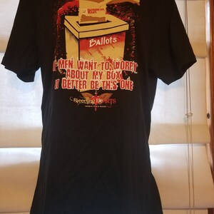 May include: Black t-shirt featuring a graphic of a hand dropping a ballot into a box labelled "Ballots". The ballot has a tick next to "Reproductive Rights". The text on the shirt reads "If men want to worry about my box, it better be this one." Below the graphic is the text "Bleeding Hearts Rebels for a Cause."