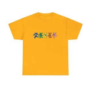 May include: A mustard yellow short-sleeve t-shirt featuring a graphic print of five stylized dancing bears in a horizontal row. The bears are colored blue, green, yellow, orange, and pink, each depicted in a mid-stride walking or dancing pose.