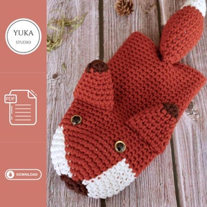 Könnte beinhalten: Eine gehäkelte Handyhülle in Form eines Fuchses in Rot, Weiß und Braun. Die Hülle hat einen weißen Bauch, braune Ohren und einen braunen Schwanz. Die Augen sind schwarze Knöpfe.