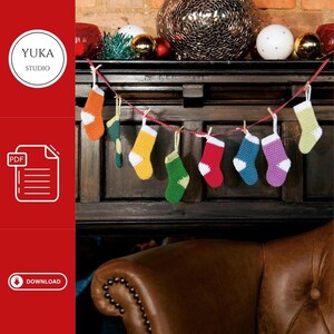 May include: A string of colourful crocheted Christmas stockings hanging from a fireplace mantel. The stockings are in shades of red, green, yellow, blue, and purple. The text "YUKA STUDIO" is visible in the top left corner of the image.