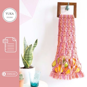 May include: A pink and orange macrame hanging fruit basket with a wooden frame. The basket is filled with oranges and limes. The basket is hanging from a hook on a white wall. The text "YUKA STUDIO" is visible in the top left corner of the image. The text "PDF" is visible in the bottom left corner of the image. The text "DOWNLOAD" is visible in the bottom left corner of the image.