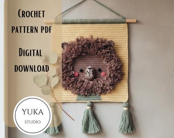 May include: A crochet lion wall hanging with a textured brown mane, pink cheeks, and a detailed face. The wall hanging is yellow and has green tassels at the bottom. The text "CROCHET PATTERN PDF DIGITAL DOWNLOAD" is visible.