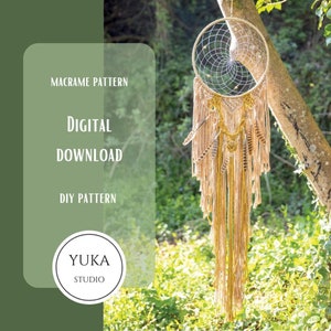 May include: A digital download pattern for a macrame dreamcatcher with beige and gold yarn, feathers, and beads. The pattern is available for DIY projects and is called "Yuka Studio".