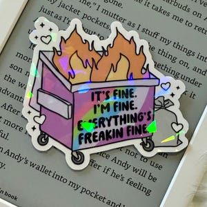 Puede incluir: Una pegatina holográfica que representa un contenedor de basura de dibujos animados en llamas. El contenedor es morado con ruedas negras y las llamas son naranjas y amarillas. El texto de la pegatina dice: "IT'S FINE. I'M FINE. EVERYTHING'S FREAKIN FINE."