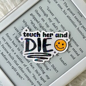 May include: A holographic sticker with the text "touch her and die" in black with rainbow glitter. A yellow smiley face sticker is next to it. The sticker is on a white e-reader.