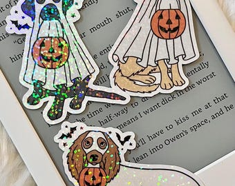 May include: Three holographic stickers of dogs dressed as ghosts for Halloween. Each dog is holding a jack-o-lantern. The stickers are on a white background.