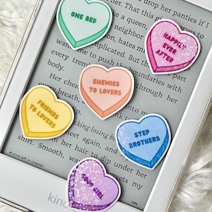 May include: A set of ten heart-shaped stickers with various sayings, including "One Bed", "Happily Ever After", "Enemies to Lovers", "Friends to Lovers", "Step Brothers", and "Good Girl". The stickers are printed on a white background and have a glossy finish.