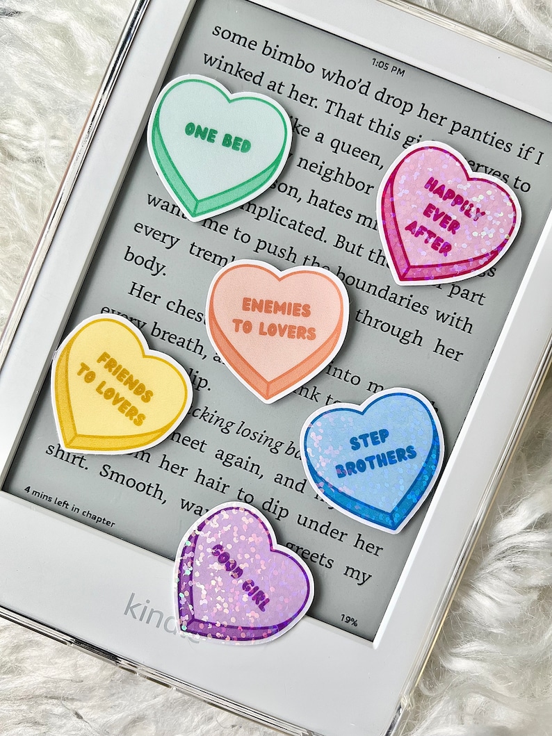 May include: A set of ten heart-shaped stickers with various sayings, including "One Bed", "Happily Ever After", "Enemies to Lovers", "Friends to Lovers", "Step Brothers", and "Good Girl". The stickers are printed on a white background and have a glossy finish.