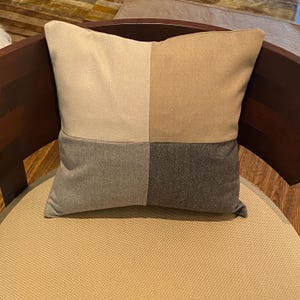 May include: A square-shaped throw pillow with a patchwork design. The pillow is made of four different fabrics in beige, light brown, gray, and dark gray.