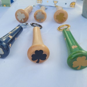 May include: Six wooden bottle openers with different colored shamrock designs. The openers are shaped like baseball bats.