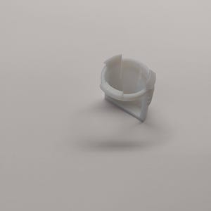 Pu&ograve; includere: Un piccolo componente in plastica bianca con un'apertura circolare e una base triangolare. L'oggetto ha una superficie liscia e sembra far parte di un meccanismo o dispositivo pi&ugrave; grande. Il design &egrave; semplice e funzionale.