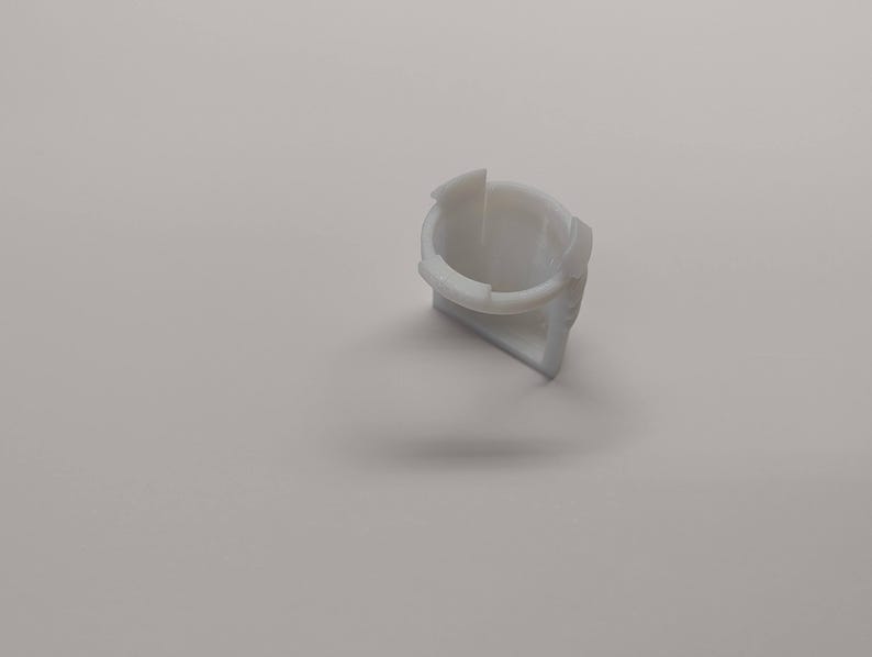 Pu&ograve; includere: Un piccolo componente in plastica bianca con un'apertura circolare e una base triangolare. L'oggetto ha una superficie liscia e sembra far parte di un meccanismo o dispositivo pi&ugrave; grande. Il design &egrave; semplice e funzionale.