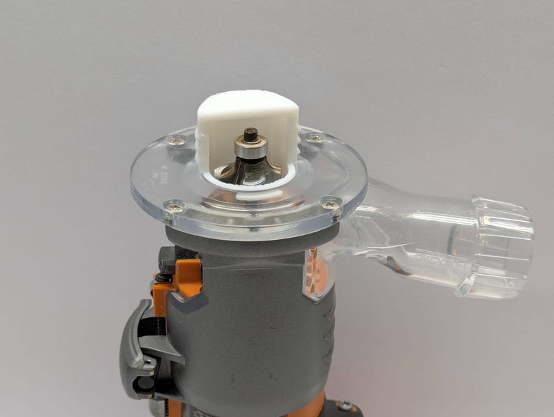 Pu&ograve; includere: Un elettroutensile grigio e arancione con una base in plastica trasparente e una parte superiore bianca. L'utensile ha una porta di raccolta della polvere in plastica trasparente. Progettato per la lavorazione del legno e altri progetti fai-da-te.