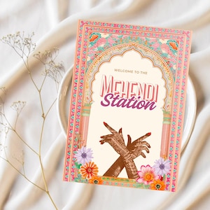 May include: A sign with a pink, orange, and blue floral border and a white background. The sign says "Welcome to the Mehndi Station" in a pink and gold font. Two hands with henna designs are crossed in front of the text.