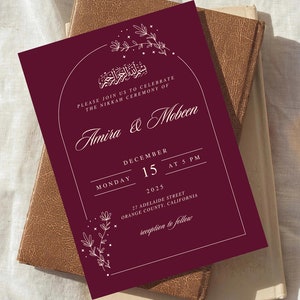 May include: A burgundy wedding invitation with white calligraphy announcing the Nikkah ceremony of Amira & Mobeen on Monday, December 15th, 2025 at 5 PM. The invitation includes the address and details about the reception to follow.