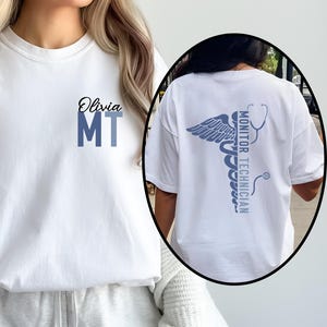May include: White t-shirt with the name "Olivia" and "MT" in blue on the front. The back of the shirt features a medical caduceus design with the words "Monitor Technician".
