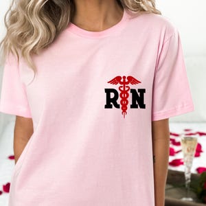 May include: Pink t-shirt with a black "RN" graphic and a red medical symbol.
