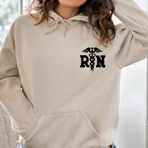 May include: A beige hoodie with a black  "RN" graphic and a caduceus symbol.