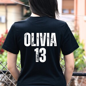 May include: Black t-shirt with white text that says "Olivia 13" on the back.