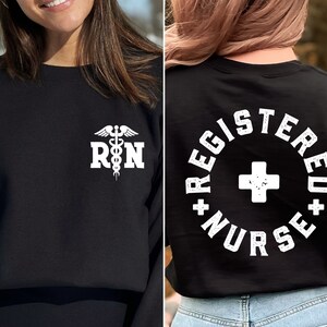 May include: Black sweatshirt with a white graphic of a medical caduceus and the letters "RN" on the front. The back of the sweatshirt has a white circle with the text "REGISTERED NURSE" and a white plus sign in the center.