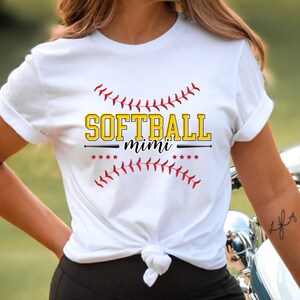 May include: White t-shirt with a red and yellow graphic that says "Softball mimi" with a baseball bat and stitching around the text.
