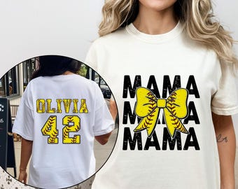 May include: White t-shirt with black text that says "Mama" three times with a yellow and brown softball bow in between each word. The shirt also has a black number "42" and the name "Olivia" in black text.