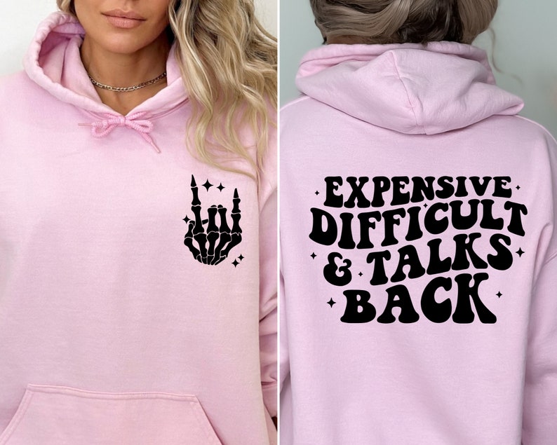 K&ouml;nnte beinhalten: Rosafarbener Hoodie mit einer schwarzen Skeletthand, die ein Rock'n'Roll-Zeichen auf der Vorderseite macht, und dem Text "EXPENSIVE DIFFICULT & TALKS BACK" auf der R&uuml;ckseite.