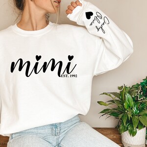 May include: White sweatshirt with black text that reads "mimi est. 1992" with two small black hearts above the text. The left sleeve has black text that reads "Cheryl Olivia" with a small black heart above the text.