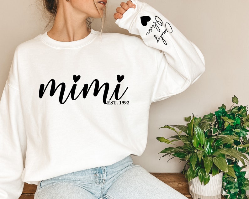 May include: White sweatshirt with black text that reads "mimi est. 1992" with two small black hearts above the text. The left sleeve has black text that reads "Cheryl Olivia" with a small black heart above the text.