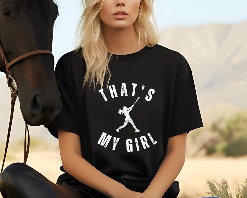 May include: Black t-shirt with a white graphic of a girl playing baseball and the text "That's My Girl".