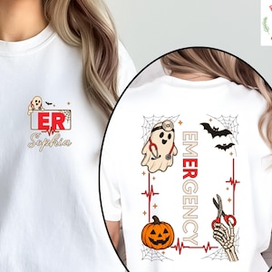 May include: A white t-shirt featuring a small chest graphic of a ghost with a stethoscope and the text ER Sophia. The back graphic displays a ghost, a pumpkin, a skeleton hand holding scissors, bats, spiderwebs, and the word EMERGENCY.