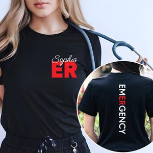May include: Black t-shirt with the text "Sophia ER" in red on the front and "EMERGENCY" in white on the back. The shirt is being worn by a person with a stethoscope around their neck.