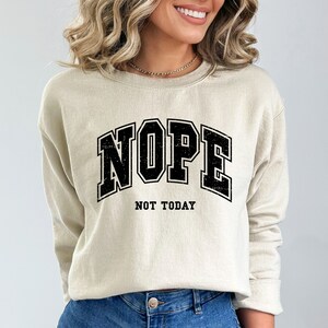 May include: A beige sweatshirt with a black graphic print that says "NOPE NOT TODAY" in a vintage collegiate style font.