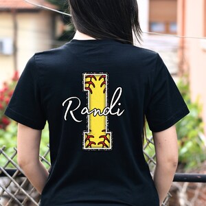 May include: Black t-shirt with a yellow and red softball letter I and the name "Randi" in white cursive writing.